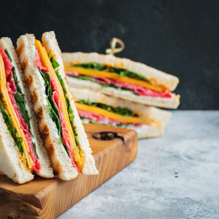 Two homemade sandwiches with sausage, cheese and arugula on a light concrete background. The concept of a quick meal or snack at work or school. With copy space